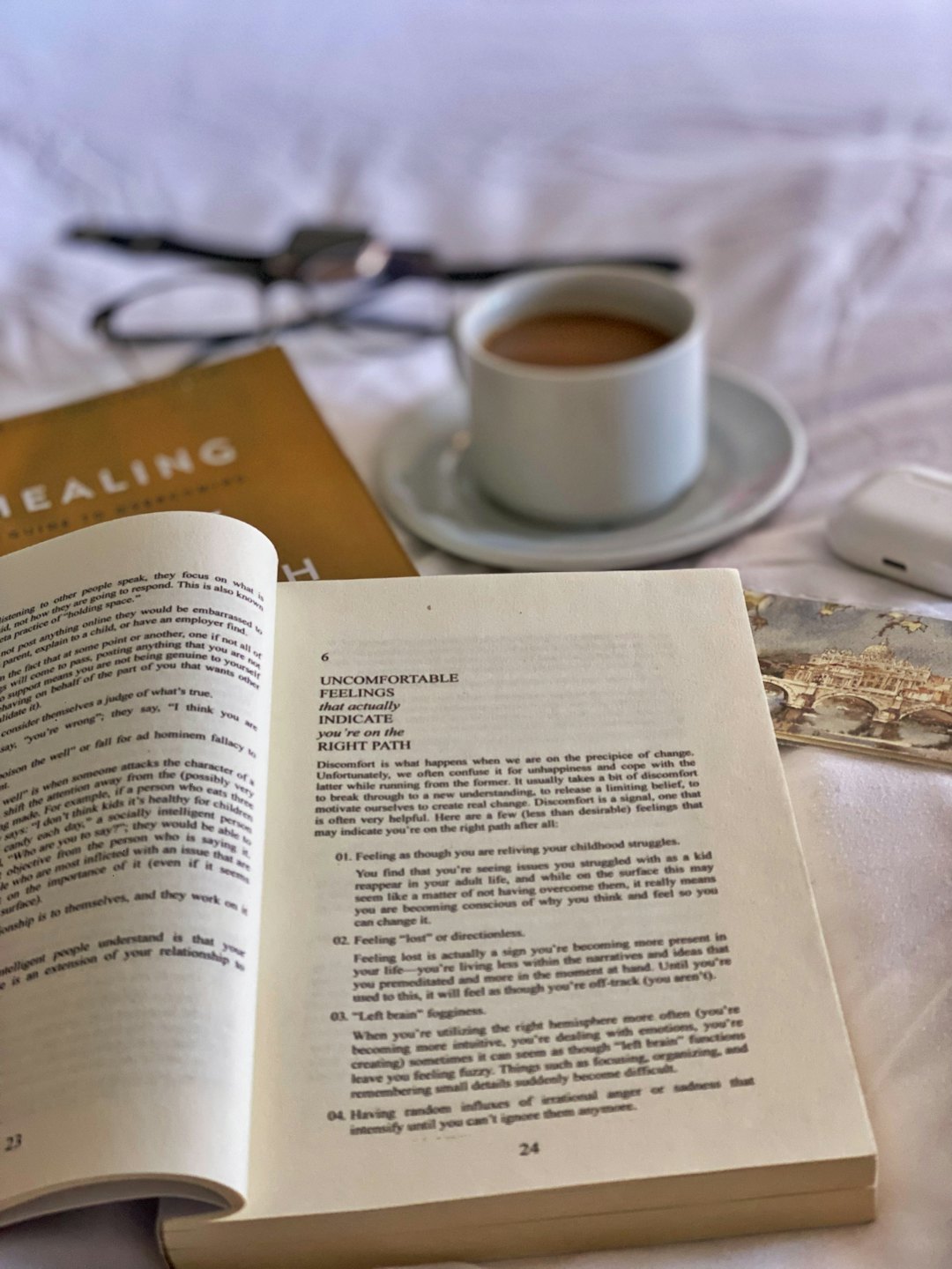 Libro abierto titulado SANACIÓN con café y gafas sobre ropa de cama blanca.