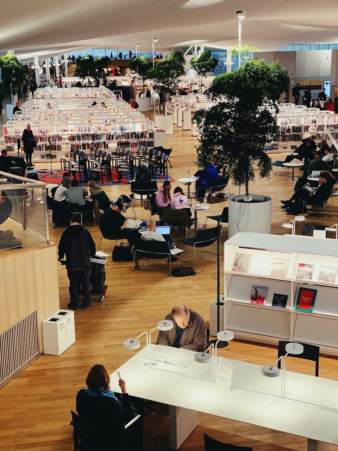 Gente leyendo y trabajando en una biblioteca moderna y luminosa de varios niveles.