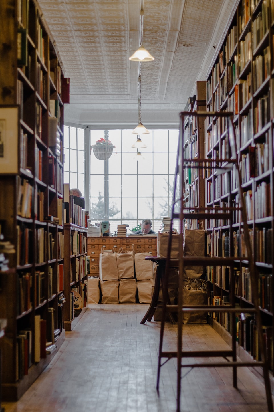 Pasillo de librería con estanterías de madera que conducen a un mirador donde alguien lee.