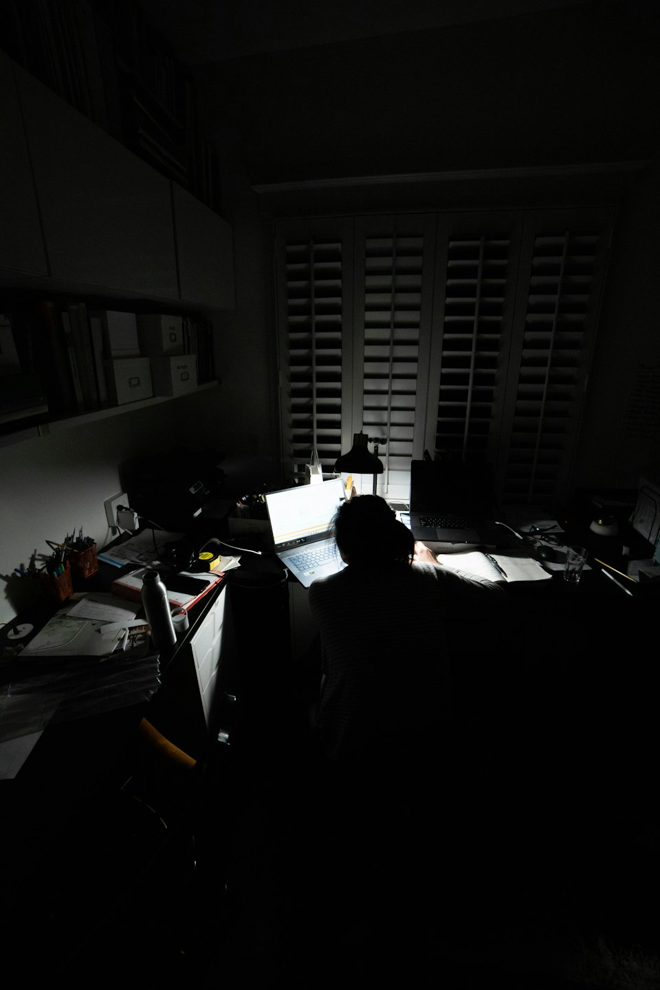 Persona trabajando en un portátil en un escritorio desordenado en una habitación oscura.